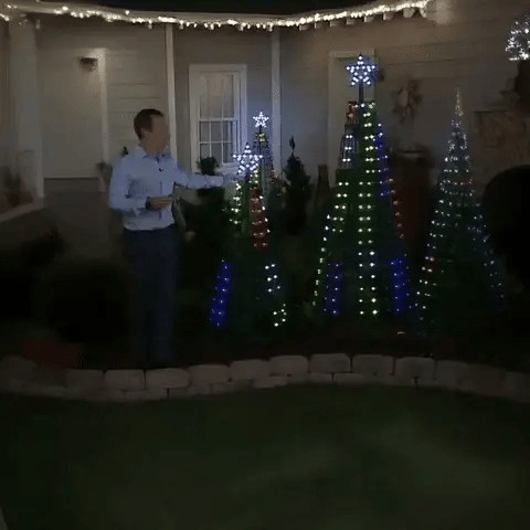 Man using the remote control on a yard display of five light show trees